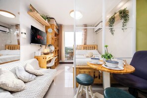 A modern, well-lit room with a TV, wooden furniture, a dining area, and a view through a glass wall. - Cozy Wood-cabin Studio With Balcony & Warm Lighting (Lapu-Lapu)