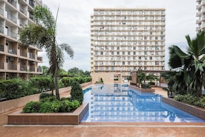 A high-rise residential building with multiple balconies, a central swimming pool, and surrounding greenery. - Cozy Wood-cabin Studio With Balcony & Warm Lighting (Lapu-Lapu)