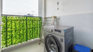 Pyykkitila, jossa on pesukone, pyykkiteline ja viherkasvi ikkunan lähellä.
