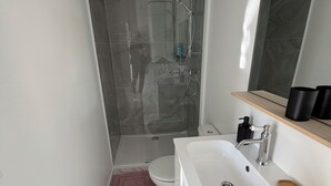 Une salle de bain moderne avec une douche à l’italienne en verre, un lavabo blanc agrémenté d’un plateau en bois et un sol en marbre.