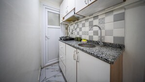 Una cocina compacta con armarios blancos, encimera de granito, pileta y un salpicadero con diseño.