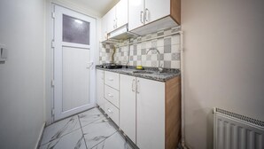 Cocina compacta con armarios blancos, salpicadero de azulejos, ventana y radiador.