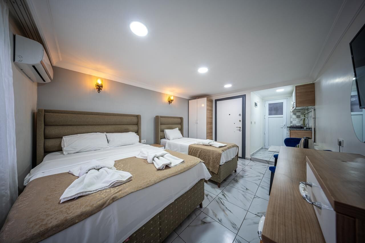 A hotel room with two beds, a wooden dresser, a bathroom, and a kitchenette.