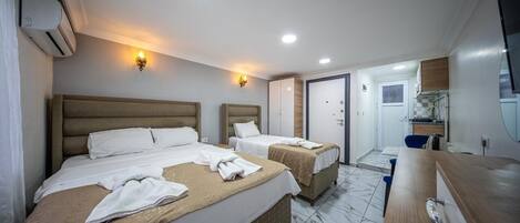 A hotel room with two beds, a wooden dresser, a bathroom, and a kitchenette.