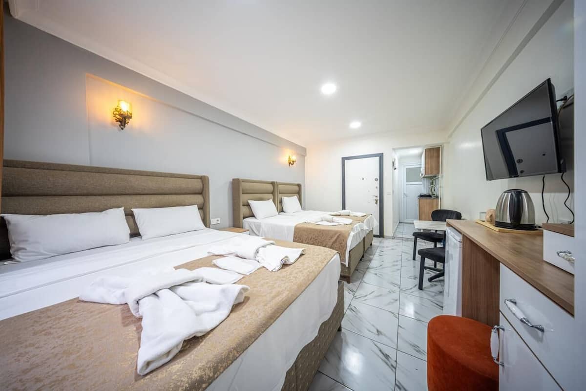 A hotel room with three beds, a desk, a television, and a bathroom visible in the background.