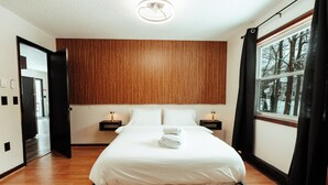 Ein modernes Hotelzimmer mit einem großen Bett, einer Wandpaneinung aus Holz, Nachttischen mit Lampen und einem Fenster mit Blick auf Bäume.