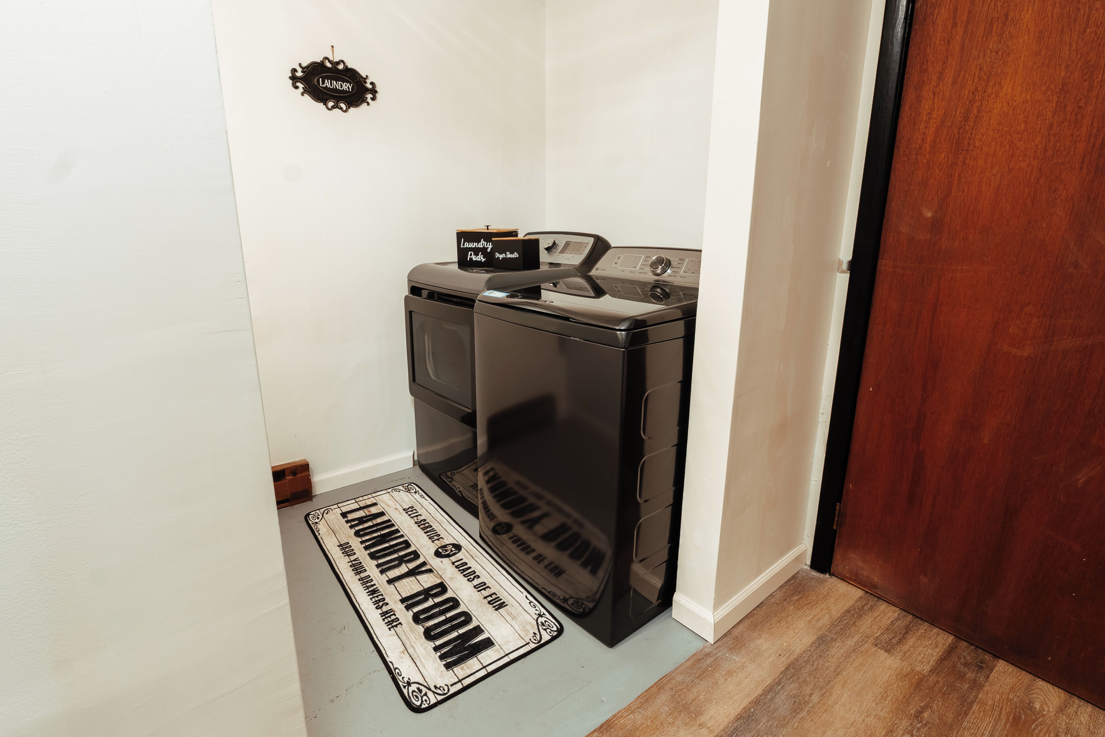 Una lavandería con lavadora y secadora, un felpudo de madera y un letrero que dice 'Laundry Room'.