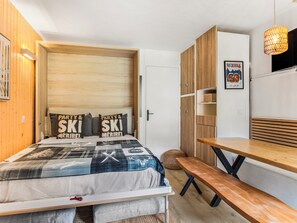Un dormitorio pequeño con cama, un banco, un armario de madera y una lámpara colgante.