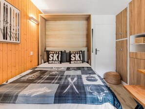 Ein Schlafzimmer mit einem Bett, einem Holzkopfteil, Skiern an der Wand und Kissen mit Ski-Motiv.