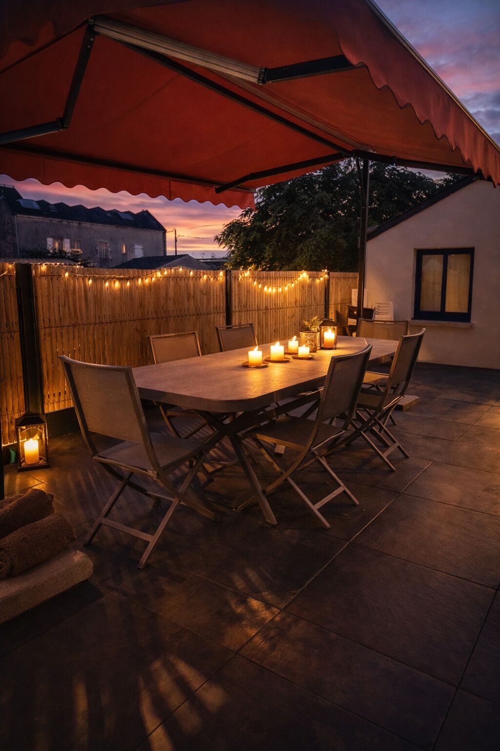 Eine Terrasse im Freien mit einem Holztisch, Stühlen, Lichterketten und Kerzen.