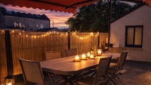Eine Terrasse im Freien mit einem Holztisch, Stühlen, Lichterketten und Kerzen.