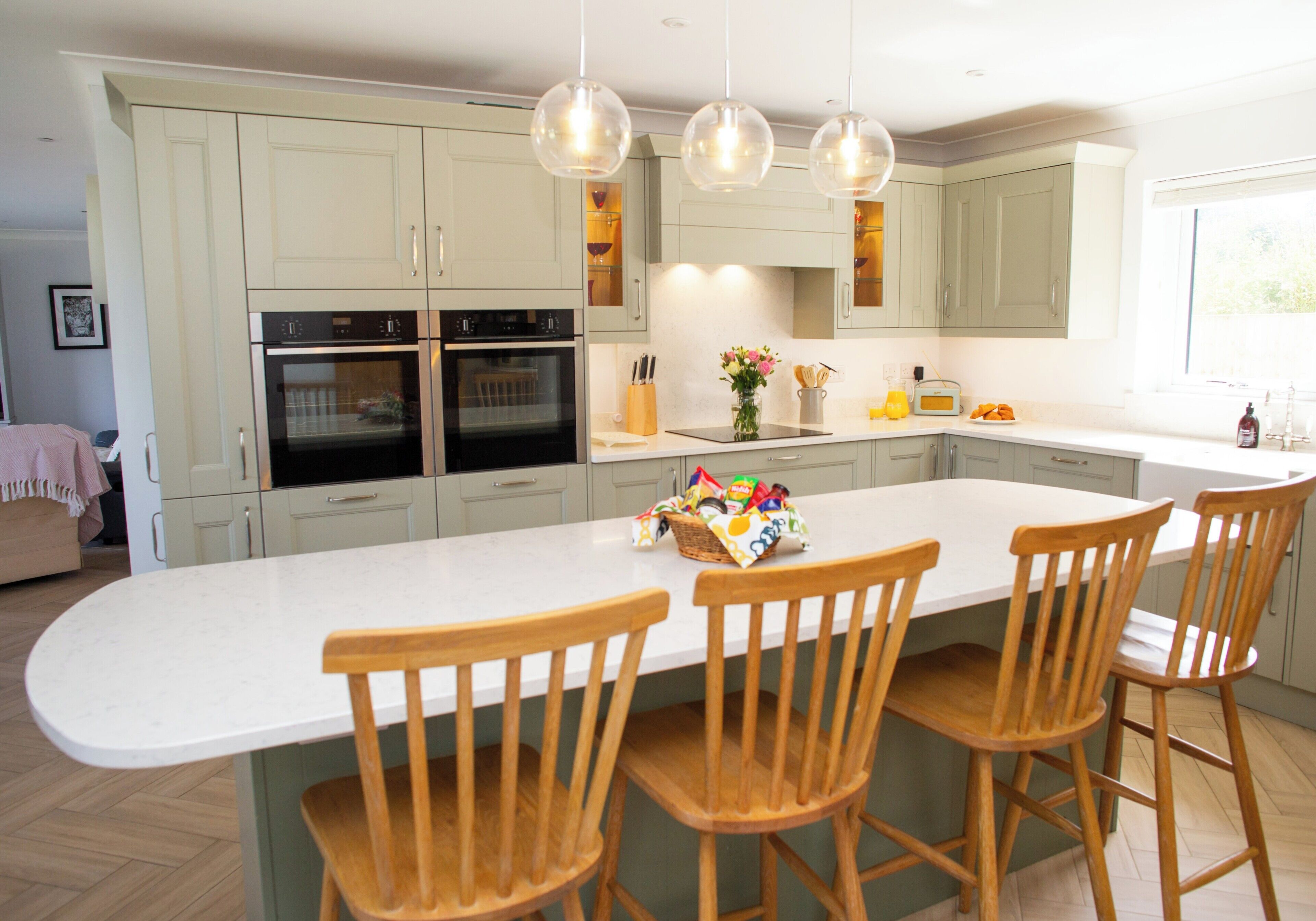 A modern kitchen with a central island, bar stools, and a double oven.