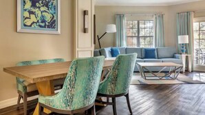 A dining area with a wooden table and green upholstered chairs, a sofa with blue cushions, and a large abstract painting on the wall. - 1 Bedroom Condo, Sleeps 4, SeaWorld Hilton Grand Vacations (Orlando)