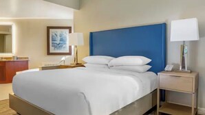 A hotel room with a bed, a nightstand, a lamp, a desk, and a framed picture on the wall. - 1 Bedroom Condo, Sleeps 4, SeaWorld Hilton Grand Vacations (Orlando)