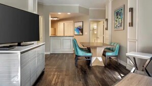 A modern kitchen with a flat-screen TV, teal chairs, and a wooden dining table. - 1 Bedroom Condo, Sleeps 4, SeaWorld Hilton Grand Vacations (Orlando)