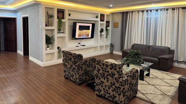 Una sala de estar moderna con un televisor de pantalla plana, sofá de cuero, sillones estampados y una mesa de centro de vidrio.