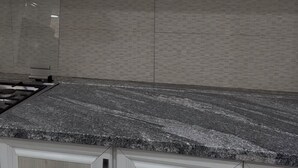 Una cocina con gabinetes blancos, encimera de granito y salpicadero de azulejos.