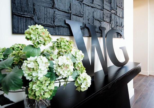 A black console table with a large 'WG' sign and a vase of green hydrangeas. - Brayden Tower Suite #05 Poolside Walk Out Patio (Lawton)