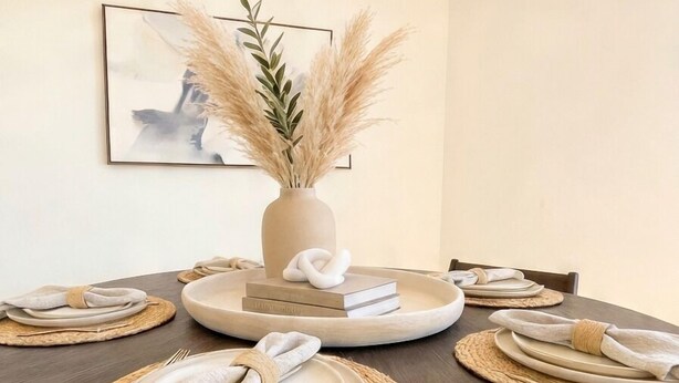 Una mesa de comedor dispuesta con platos, cubiertos y manteles individuales, rodeada de sillas.