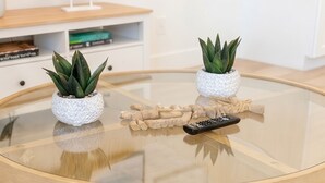 Una mesa de centro redonda de vidrio con dos plantas en macetas y un control remoto.