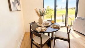 Un comedor con una mesa redonda, sillas, un jarrón con plantas secas y vistas a un espacio exterior a través de puertas de cristal grandes.