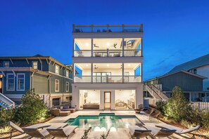 Ein mehrgeschossiges Haus mit Swimmingpool, Sitzgelegenheiten im Freien und einer Treppe, die zu den oberen Stockwerken führt.