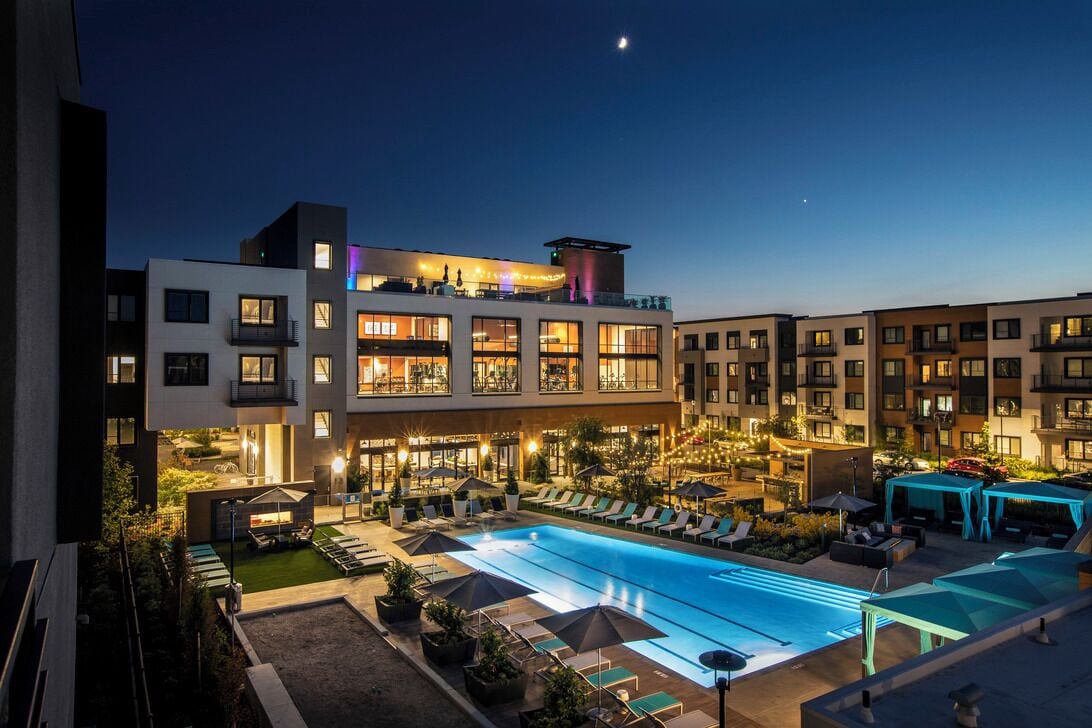Een modern hotel met een zwembad op het dak, meerdere balkons en zitgedeeltes buiten.