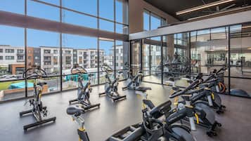 Un gimnasio moderno con varias bicicletas estáticas, grandes ventanales y vistas de edificios circundantes.