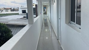 Un pasillo con paredes blancas, piso de baldosas y una ventana a la derecha.