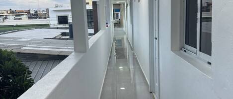 A corridor with white walls, a tiled floor, and a window on the right.