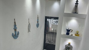 Una habitación con suelo de baldosas, una mesa con sillas, detalles decorativos en la pared y estantes con varios objetos.