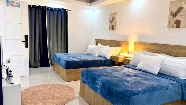 Habitación de hotel con dos camas, un escritorio pequeño, una lámpara y una puerta con un cartel.