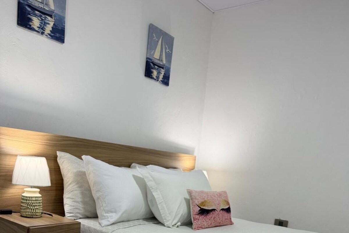 A bedroom with a wooden headboard, a bedside table with a lamp, and a bed with white bedding.