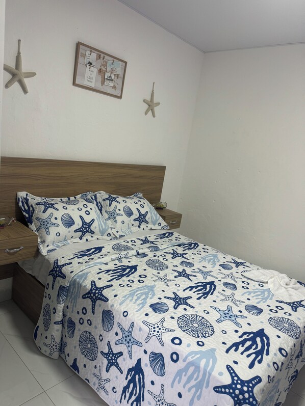 Un dormitorio con cama, cabecera de madera, dos mesitas de noche, un cuadro en la pared y adornos de estrella de mar.