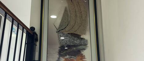 A framed artwork of a sailboat on water, a staircase with black railings, and a small decorative coral piece on the floor.