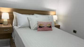 A neatly made bed with white linens, two bedside lamps, and two framed pictures on the wall.
