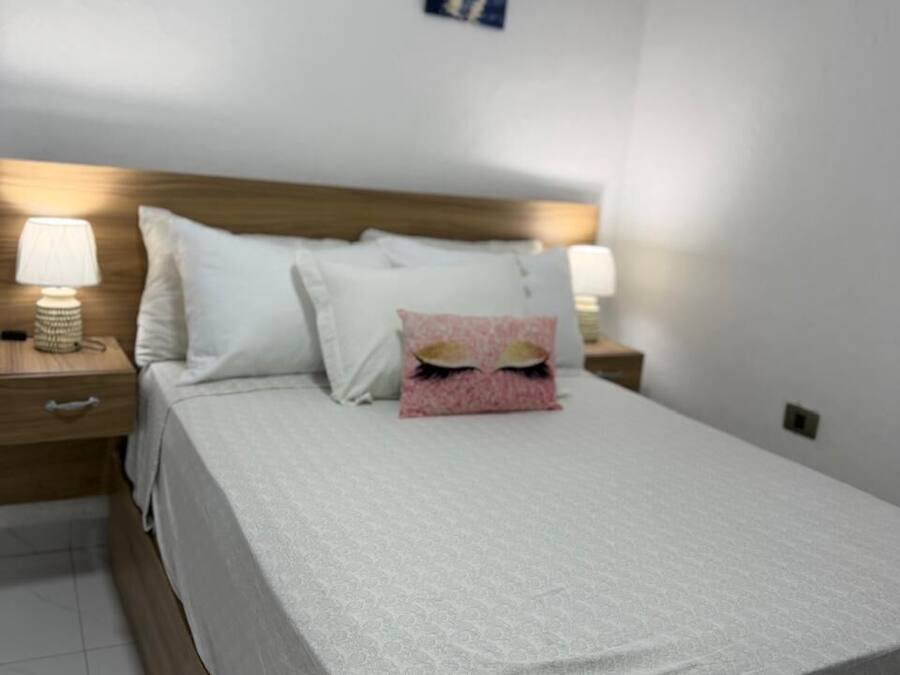 A neatly made bed with white linens, two bedside lamps, and two framed pictures on the wall.