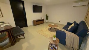 Ett vardagsrum med en soffa, ett soffbord, en tv, en växt och en matplats med ett bord och stolar.