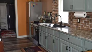 Una cocina con armarios azul claro, salpicadero de ladrillo, pileta de acero inoxidable y encimera de madera.