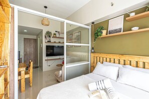 A bedroom with a bed, a TV, wooden furniture, and shelves with plants. - Nordic-inspired Rustic Minimalist Condo (Lapu-Lapu)