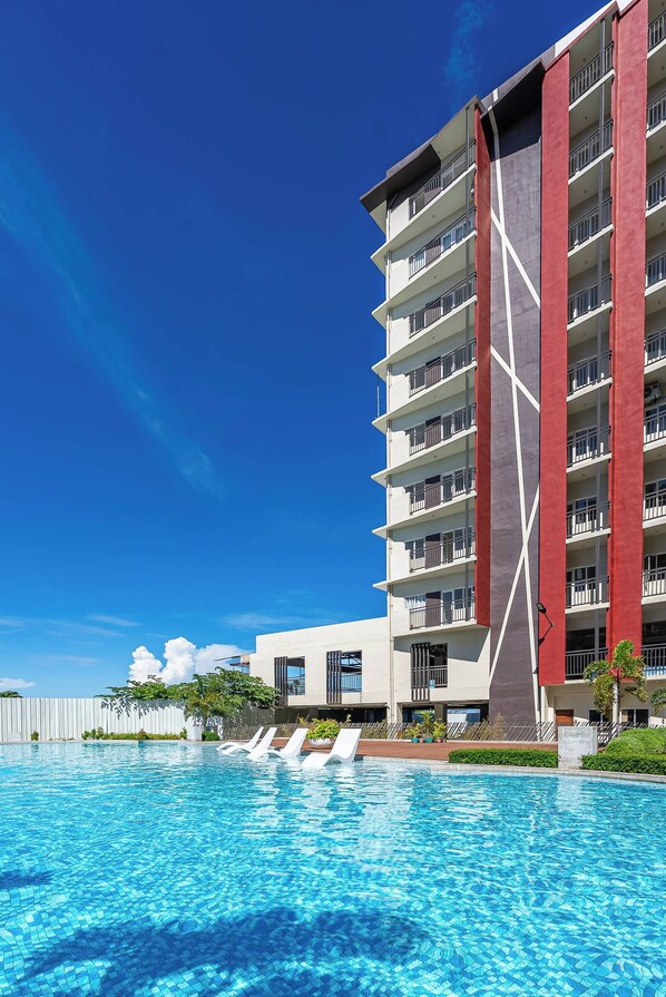 Et moderne hotel med swimmingpool, flere balkoner og en klar blå himmel.