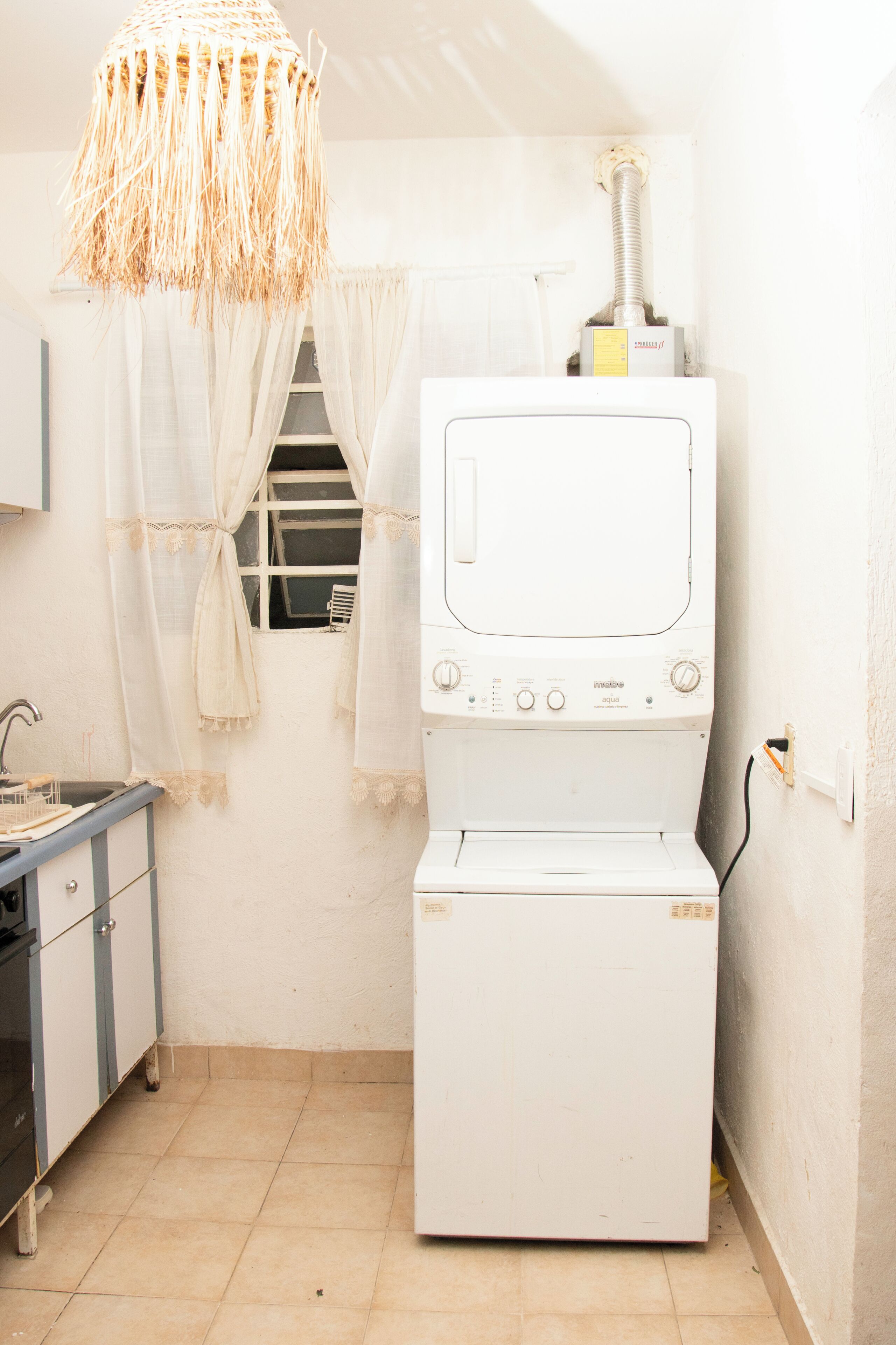 A compact laundry room with a washing machine, a sink, and a hanging rack.