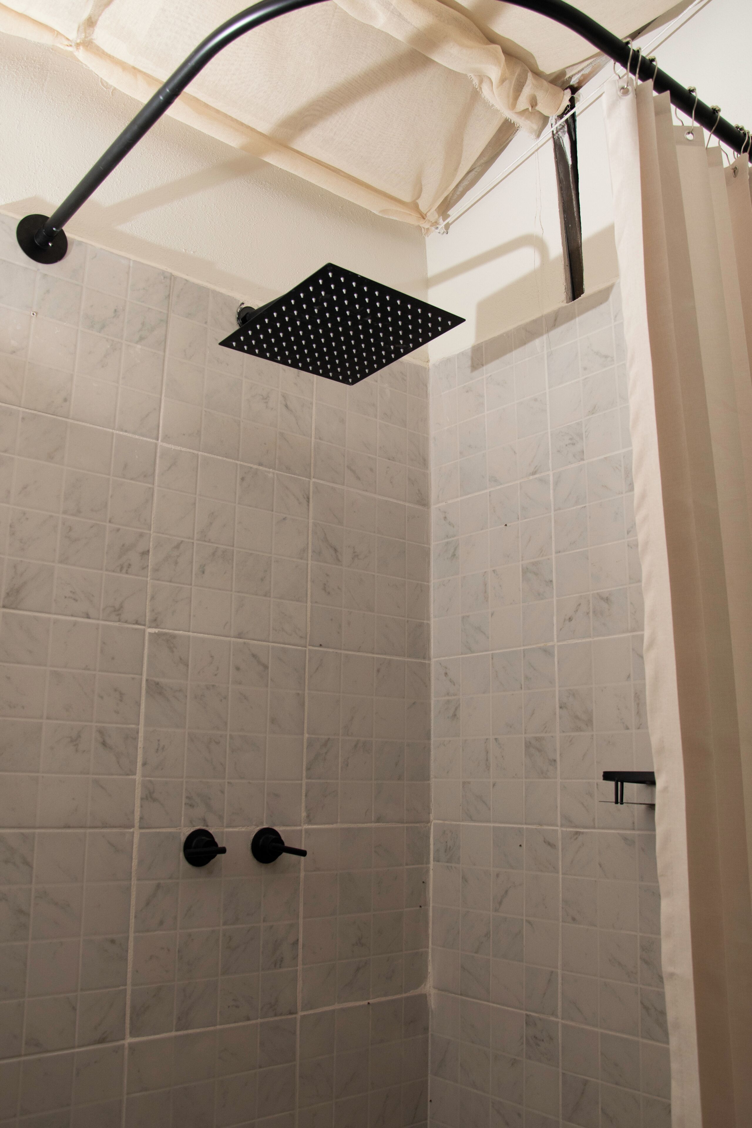 Een douche met een vierkante douchekop, een handdoekhouder en een gordijn.