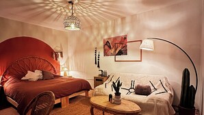 Una habitación acogedora con cama, sofá, mesa de centro, silla, lámpara, un cactus y una lámpara de techo.