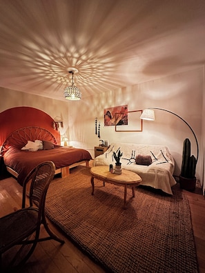 Ein gemütliches Zimmer mit Bett, Sofa, Couchtisch, Sessel, Lampe, einem Kaktus und einer Deckenleuchte.