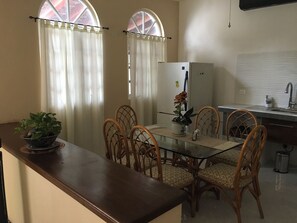 A dining area with a glass table, wicker chairs, a potted plant, a refrigerator, and a kitchen counter with a sink. - La palma Great Location Spacious Funtonal Equipied (Cancún)