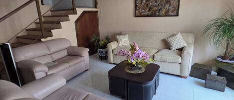 A living room with a sofa, a coffee table, a staircase, and a painting on the wall.