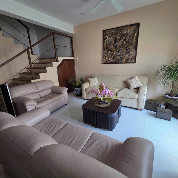 A living room with a sofa, a coffee table, a staircase, and a painting on the wall. - La palma Great Location Spacious Funtonal Equipied (Cancún)