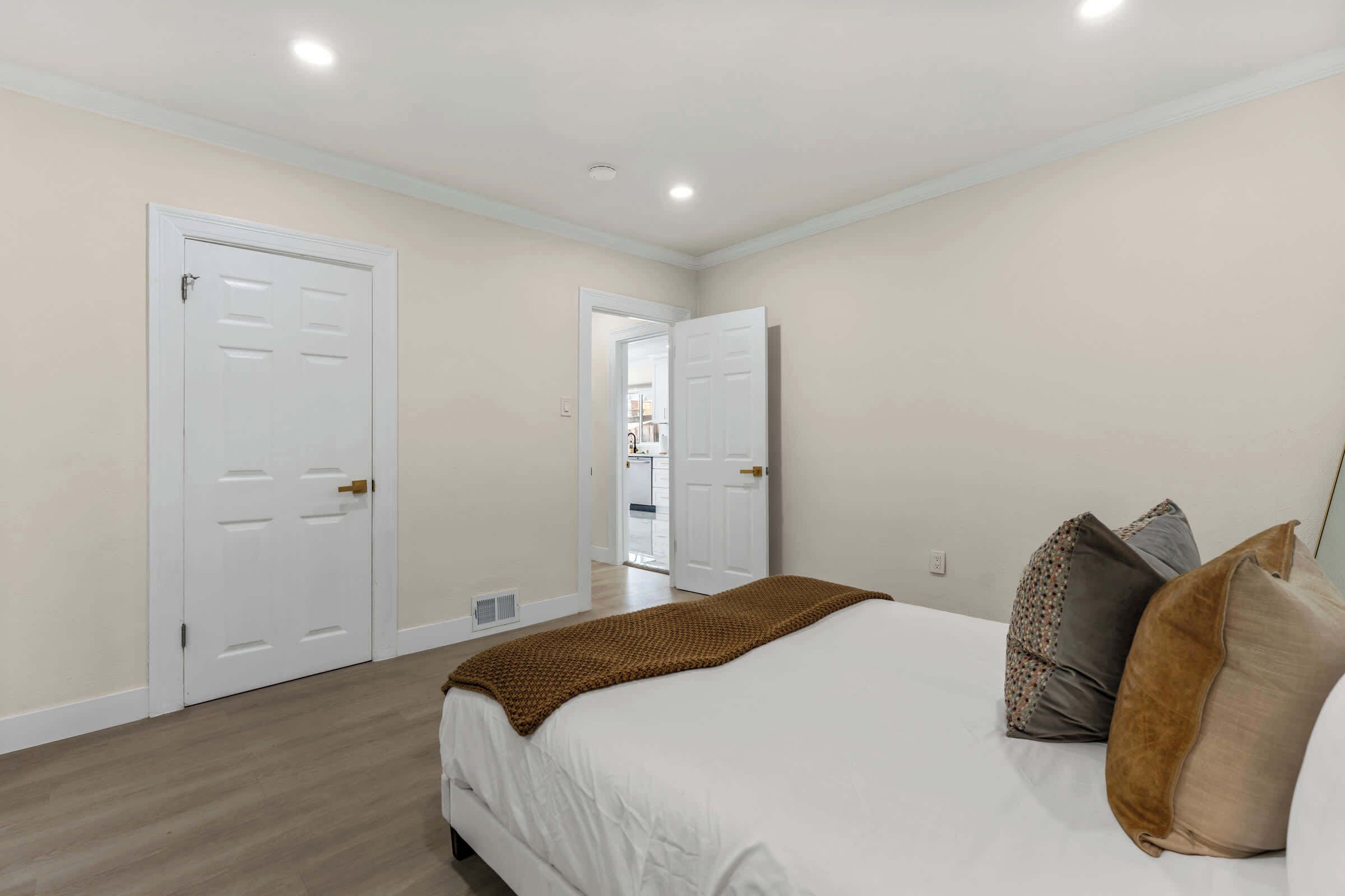Un dormitorio con una cama, dos puertas, un pasillo y un baño al fondo.