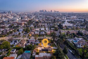 An aerial view of a residential area with a prominent yellow location marker, surrounded by houses, palm trees, and a distant city skyline.